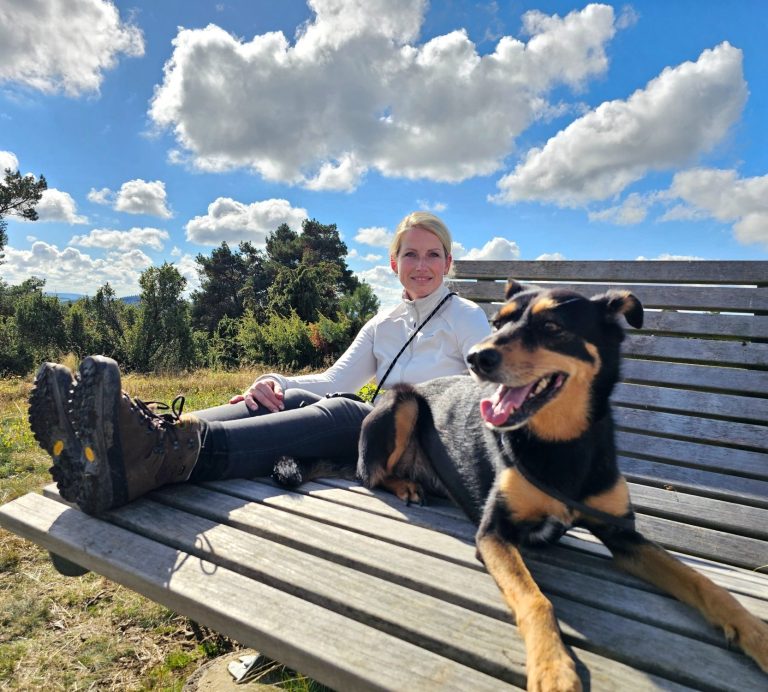 Hier sieht man Juliane Merkler von der - Tierheilpraxis akupunktierchen mit ihrer Hündin Jette auf einer Bank während einer Wanderung.